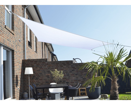Terasa se sluneční plachtou, stolem a židlemi před cihlovou budovou