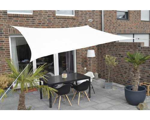 Terasa se sluneční plachtou, stolem a židlemi před cihlovou budovou