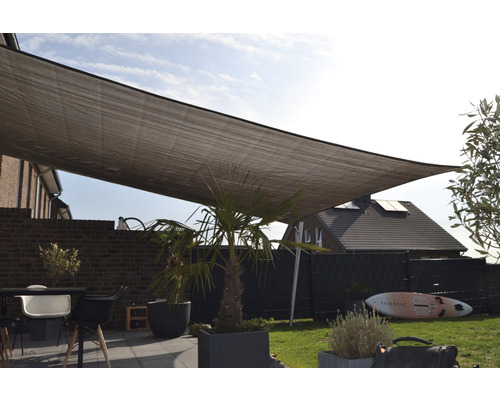 Sluneční plachta nad terasou se zahradním nábytkem a rostlinami.