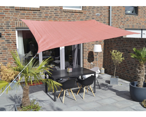 Terasa se sluneční plachtou, stůl a židle před cihlovou budovou
