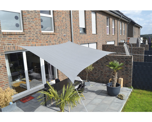 Čtvercová sluneční plachta nad terasou se stolem a rostlinami