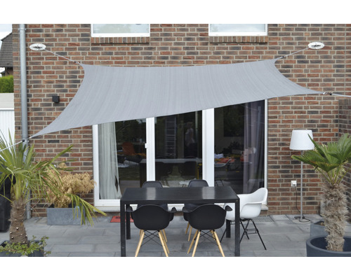 Terasa se sluneční plachtou, stůl a židle před stěnou domu