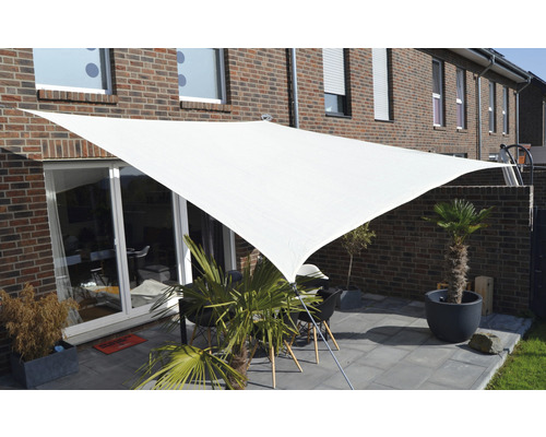 Terasa s trojúhelníkovou sluneční plachtou a zahradním nábytkem před cihlovým domem