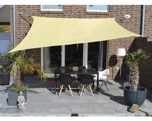 Terasa se sluneční plachtou, stolem a židlemi před cihlovou budovou