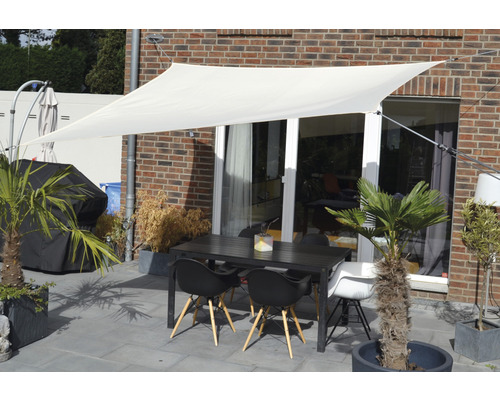 Terasa se sluneční plachtou, zahradním stolem a židlemi před stěnou domu