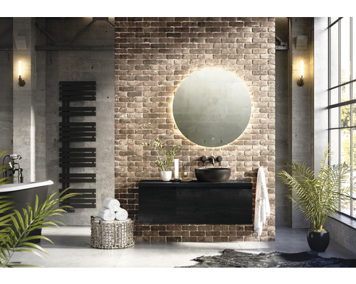 Moderní koupelna s volně stojící vanou, radiátorem na ručníky, skříňkou pod umyvadlo, kulatým zrcadlem s osvětlením a cihlovou zdí