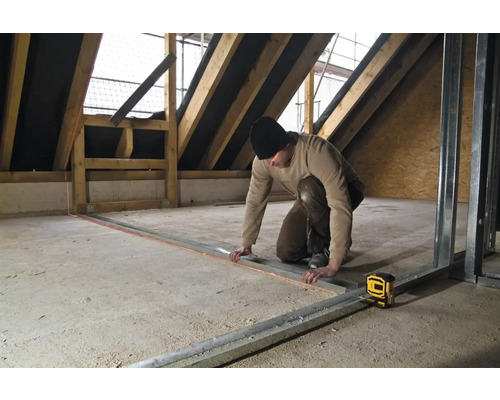 Řemeslník pracuje s čárovým laserem v podkroví na kovových profilech.