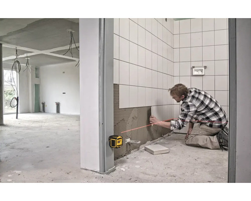 Muž pokládá dlaždice pomocí čárového laseru v nedokončené místnosti.