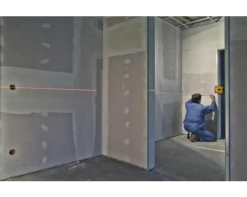 Muž používá křížový liniový laser v místnosti se sádrokartonovými stěnami k vyrovnání.