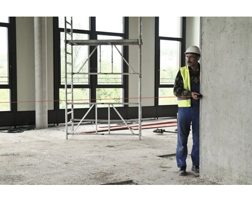 Stavební dělník s laserovým dálkoměrem v hrubé stavbě s lešením