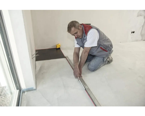 Řemeslník pokládá dlaždice s latí a nivelačním přístrojem v místnosti.