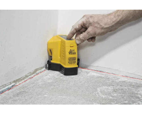 Žlutý křížový čárový laser promítá červené laserové čáry na stěnu a podlahu