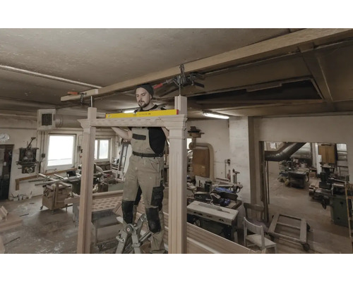 Řemeslník montuje dřevěný rám pomocí vodováhy v dílně.