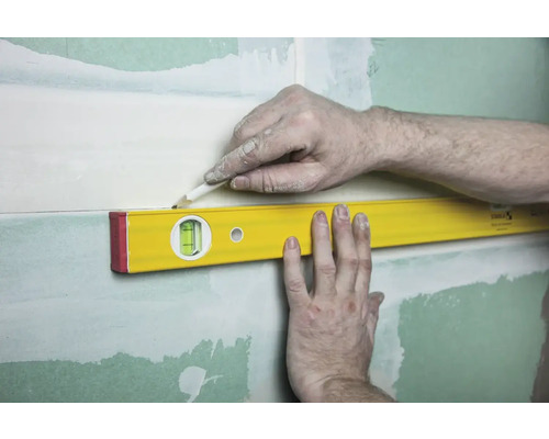 Vodováha se přikládá ke stěně se sádrokartonem, aby se tužkou nakreslila čára.