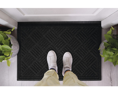 Černá rohožka s geometrickým vzorem před dveřmi