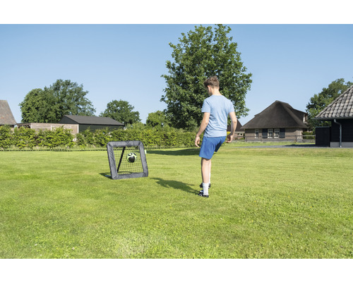 Osoba hraje fotbal s fotbalovou brankou na zahradě.