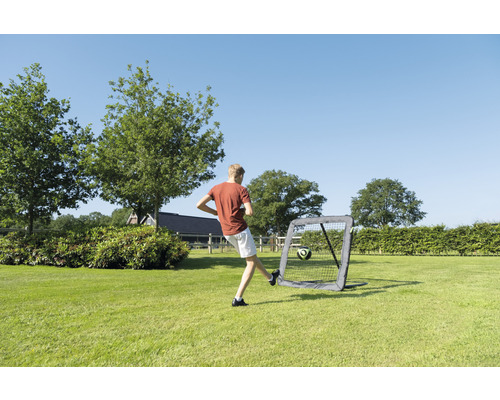 Chlapec kope fotbal do přenosné fotbalové branky na zahradě.