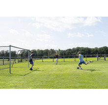 Tři děti hrají fotbal na travnatém hřišti s fotbalovou brankou.