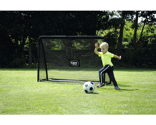 Chlapec hraje fotbal před fotbalovou brankou na zahradě.