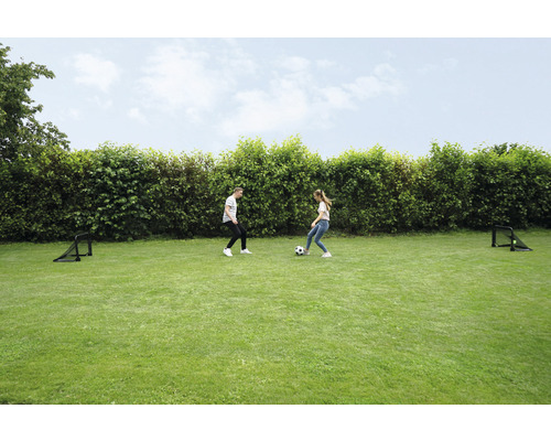 Dvě osoby hrají s fotbalovým míčem na trávníku se dvěma fotbalovými brankami.