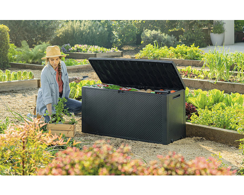 Zahradní scéna s ženou, která klečí vedle otevřeného černého zahradního boxu a sází sazenice. V pozadí je vidět zeleninová zahrada.