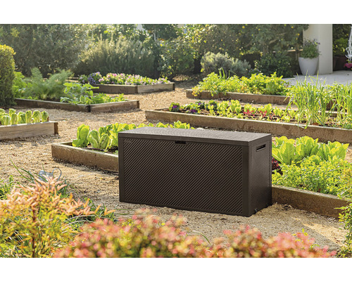 Zahradní scéna s hnědým zahradním boxem na štěrku mezi zeleninovými záhony.