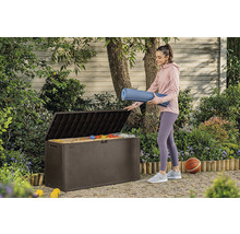 Žena ukládá podložku na jógu do hnědé zahradní bedny venku.