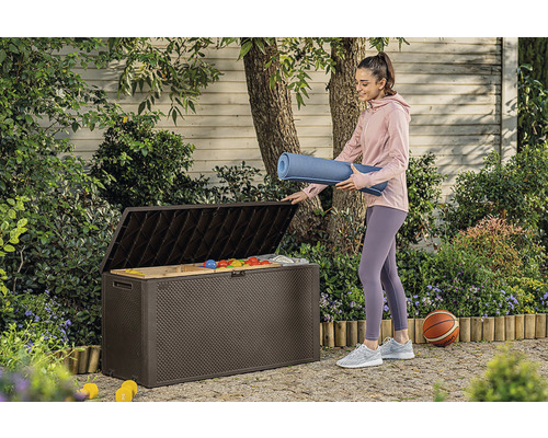 Žena ukládá podložku na jógu do hnědé zahradní bedny venku.