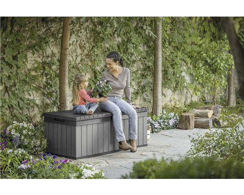 Žena a dítě sedí na šedé zahradní truhle na zahradě.