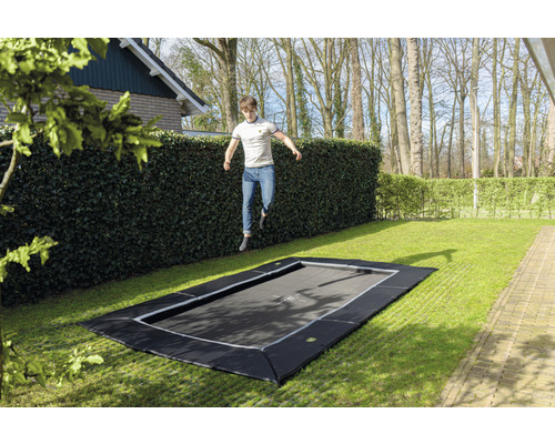 Zahradní trampolína v úrovni terénu se skákajícím mužem na zahradě