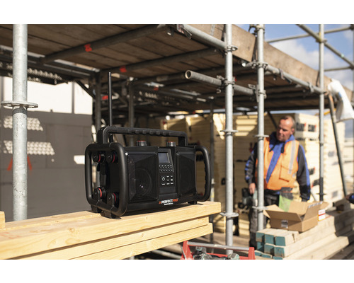 Stavební rádio na dřevěném povrchu se stavebním dělníkem v pozadí