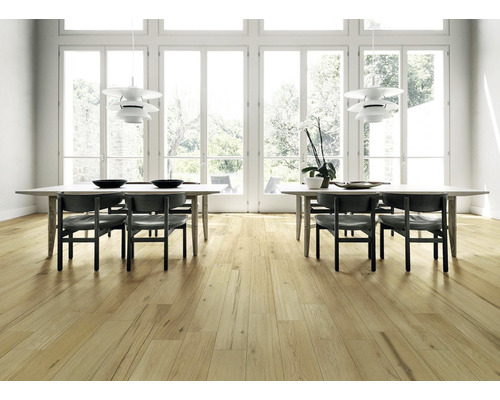 Světlá místnost s dřevěnou podlahou, jídelními stoly a židlemi pod závěsnými lampami