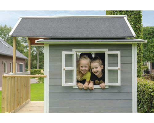 Dvě děti se dívají z okna šedého dřevěného domečku na hraní se šedou střechou