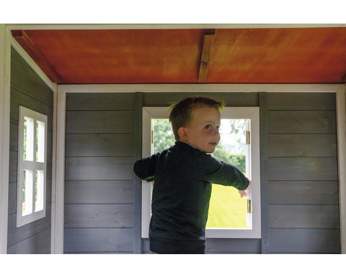 Dítě stojí v dřevěném hracím domku s okny