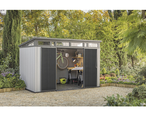 Zahradní domek s otevřenými dveřmi, umístěný na zahradě a vybavený jízdním kolem a pracovním stolem