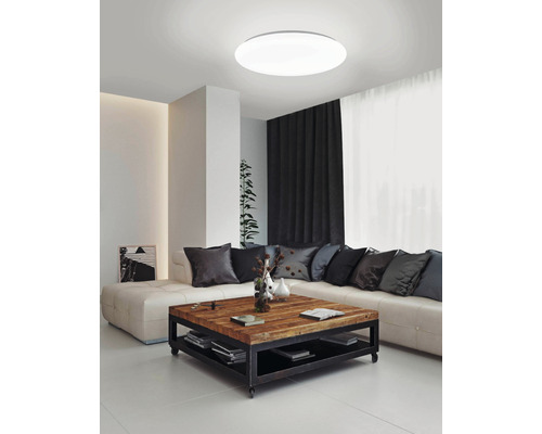 Světlý obývací pokoj s kulatým stropním svítidlem, pohovkou a dřevěným stolem