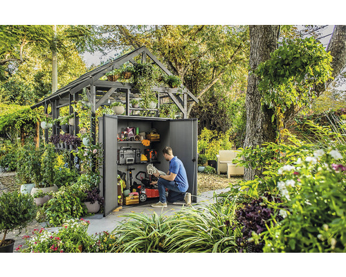 Scéna se zahradní kůlnou plnou zahradního nářadí a vybavení, obklopenou bujnou zelení