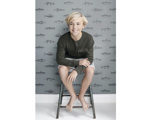 Dospívající sedí před tapetou se vzorem ryb.