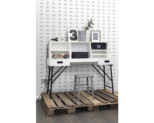 Scéna se stolem, stoličkou a dekorativními prvky před stěnou se vzorem uzlů.