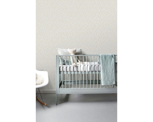 Světly dětský pokoj s tapetou s nápisy, dětskou postýlkou a houpacím křeslem.