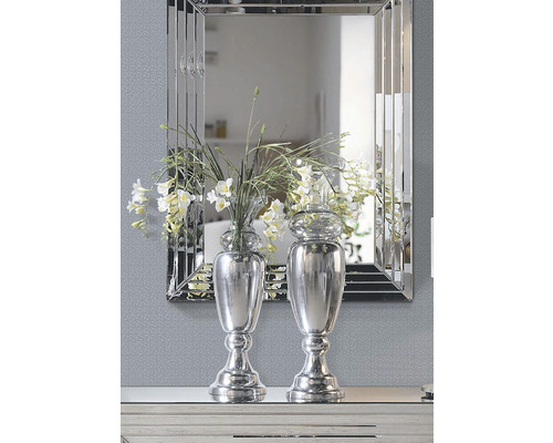 Dvě stříbrné vázy s květinami před zrcadlem.