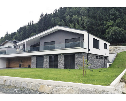 Moderní dům s kamennou fasádou a skleněným balkonem ve svahu