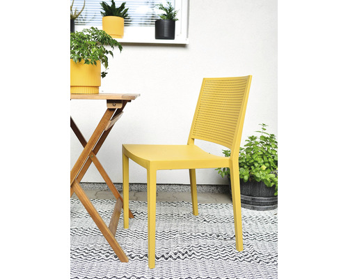 Žlutá plastová zahradní židle s perforovaným opěradlem vedle dřevěného stolu na vzorovaném koberci