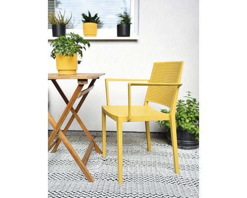 Scéna se žlutým křeslem, dřevěným stolem a rostlinami venku