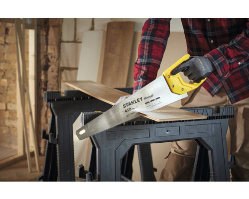 Osoba řeže dřevěnou desku ruční pilou na pracovním stole.