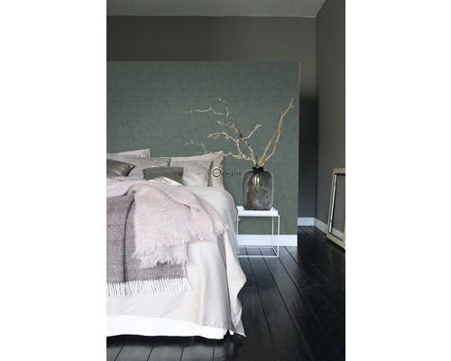 Ložnice s postelí, nočním stolkem, vázou s větvemi a vzorovanou tapetou.