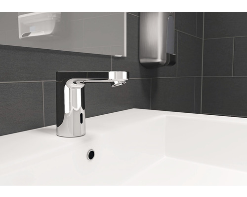 Bezkontaktní umyvadlová baterie na bílém umyvadle s tmavými obklady v pozadí