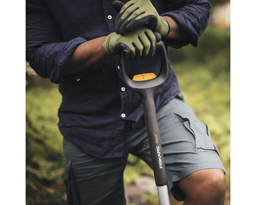 Osoba v zahradních rukavicích drží rýč značky Fiskars.