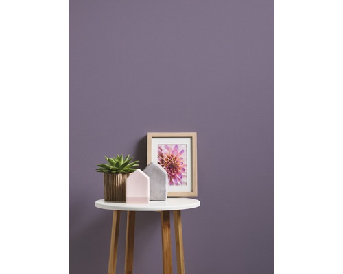 Dekorativní scéna s hrnkovou rostlinou, domácími dekoracemi a zarámovaným obrazem na malém stole před stěnou