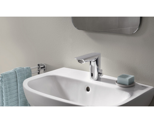 Fotografie koupelny s umyvadlem, vodovodní baterií, ručníkem a zrcadlem.